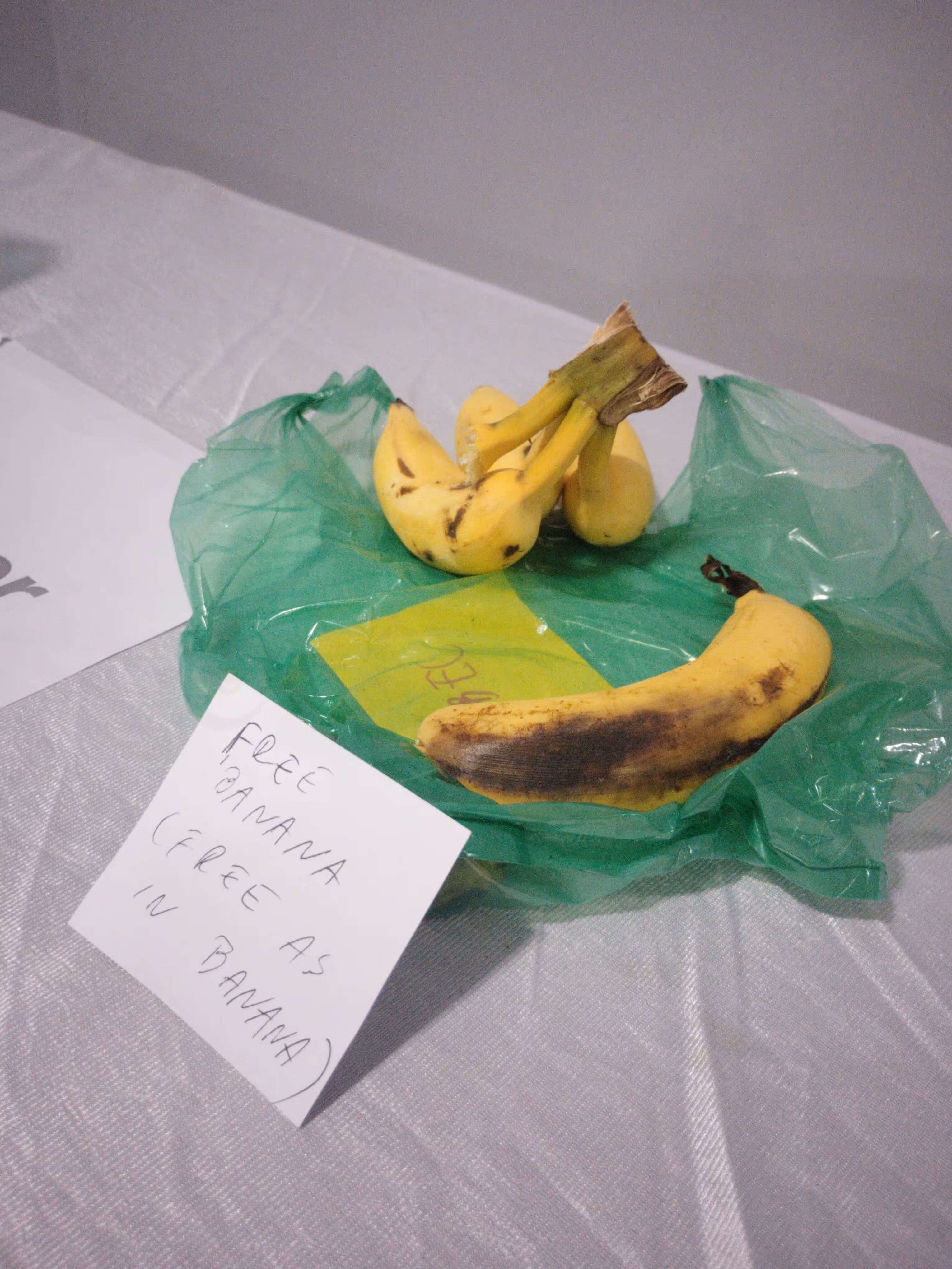 Three yellow and one mostly black banana placed on a plastic like bag.
Near the banana is a note that says &ldquo;free banana (free as in
banana)&rdquo;